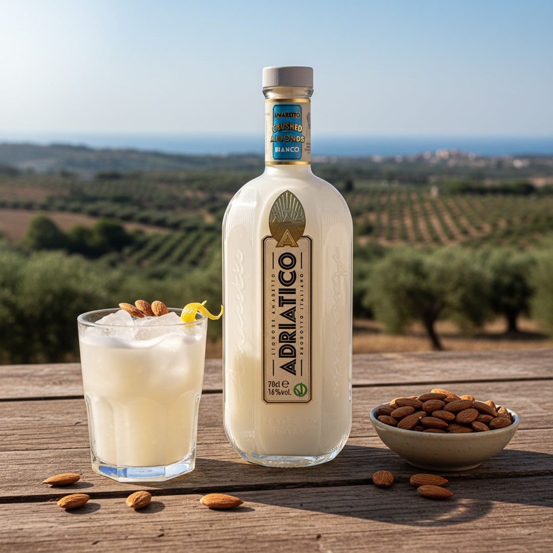 Bottle of Adriatico Amaretto Bianco with a glass of cocktail and almonds on a wooden table with a scenic background.