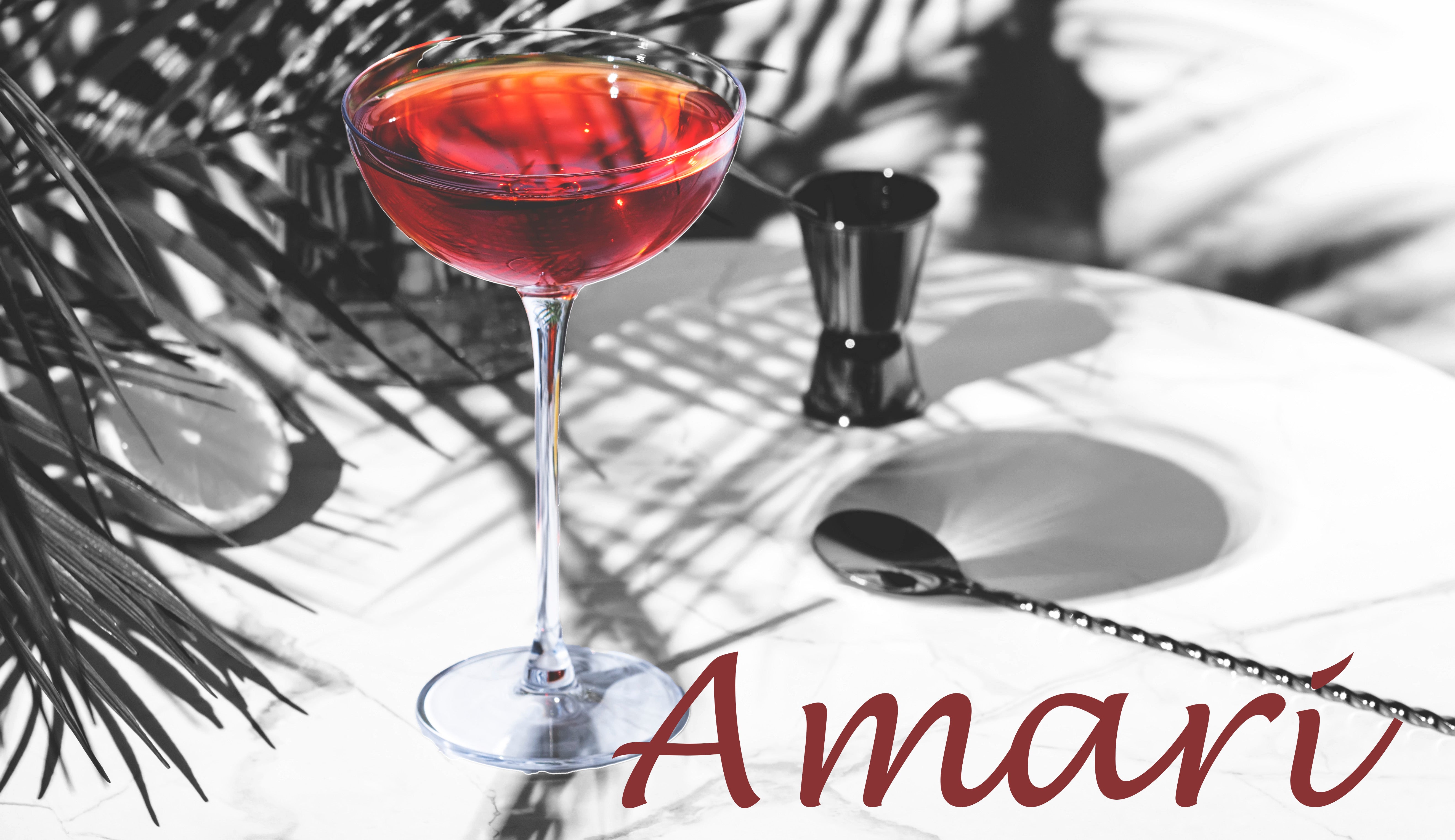 Red cocktail in a glass with 'Amari' branding on a white surface with shadows and leaves.
