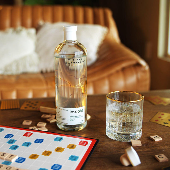 Bottle of Losophe Margarita on a table with scrabble tiles and a glass.