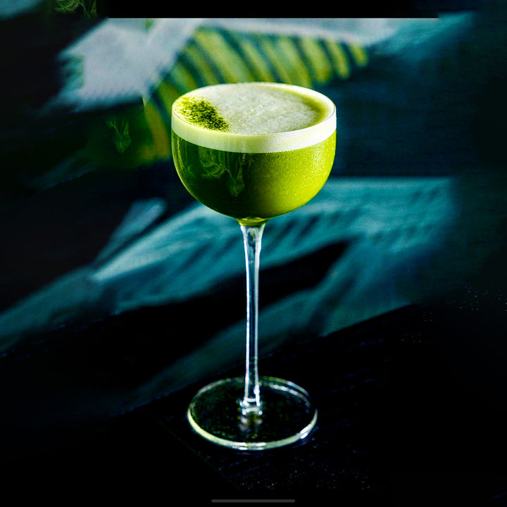 Yoshi Matcha cocktail with a white foam top in a tall glass against a dark background